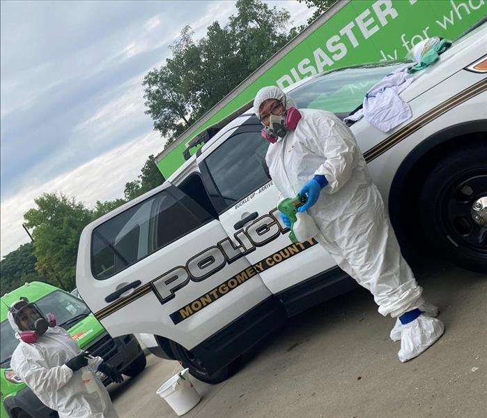 Technician in white hazmaz suit cleans police cars